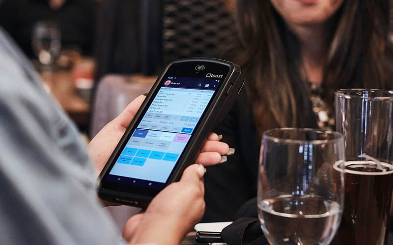 Server taking order on handheld POS device at restaurant table